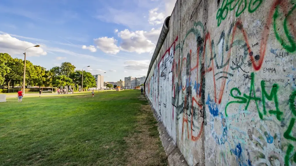 Ein langer Abschnitt der Berliner Mauer mit Graffiti und einer grünen Wiese daneben.