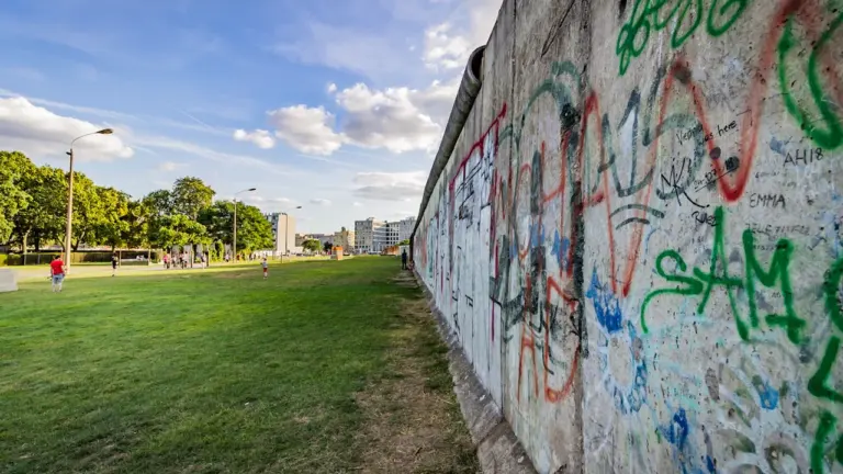 Ein langer Abschnitt der Berliner Mauer mit Graffiti und einer grünen Wiese daneben.
