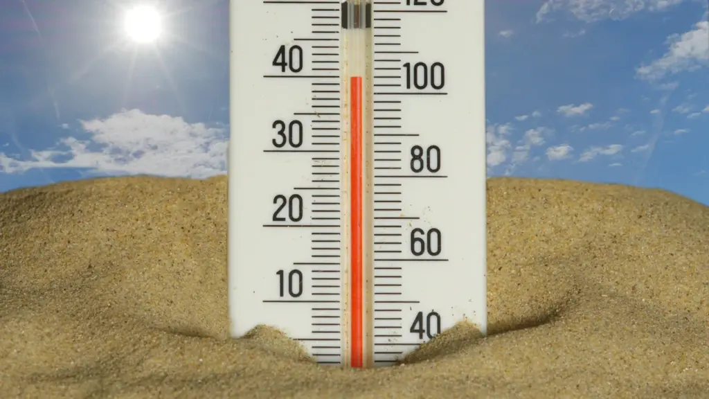 Ein Thermometer in einer Sandlandschaft zeigt bei strahlendem Sonnenschein extrem hohe Temperaturen an.