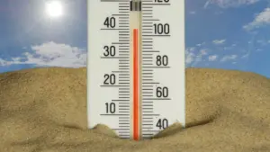 Ein Thermometer in einer Sandlandschaft zeigt bei strahlendem Sonnenschein extrem hohe Temperaturen an.