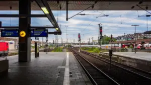 Moderner Bahnsteig mit Gleisen und digitalen Anzeigen am helllichten Tag.