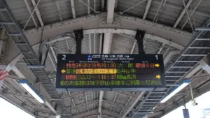 Digitale Anzeigetafel mit Zugverbindungen hängt von der Decke eines Bahnhofs.