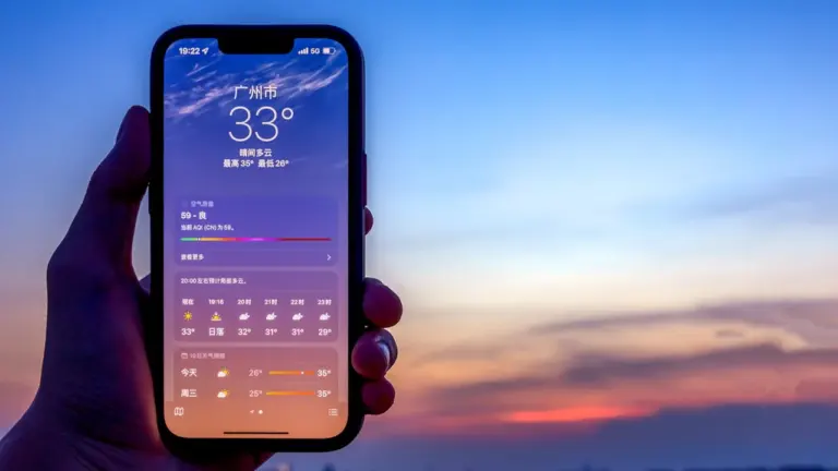 Hand hält ein Smartphone mit geöffneter Wetter-App vor einem stimmungsvollen Abendhimmel.