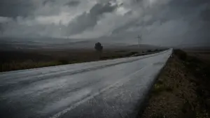 Eine regennasse Landstraße unter einem bedrohlichen, grauen und wolkenverhangenen Himmel bei schlechtem Wetter.
