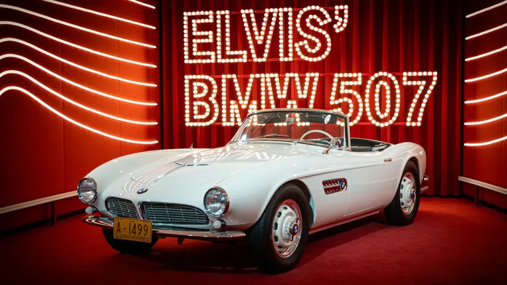 Elvis Presleys legendärer weißer BMW 507 als Ausstellungsstück auf einer roten Bühne.