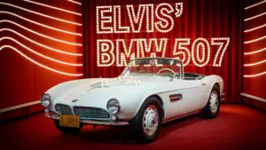 Elvis Presleys legendärer weißer BMW 507 als Ausstellungsstück auf einer roten Bühne.