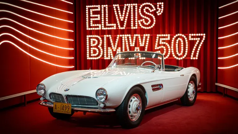 Elvis Presleys legendärer weißer BMW 507 als Ausstellungsstück auf einer roten Bühne.