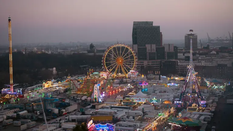 Weitwinkelaufnahme des Hamburger DOM bei Dämmerung mit leuchtendem Riesenrad und Stadtkulisse.