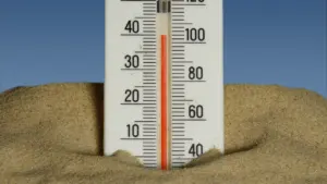 Ein Thermometer im Sand unter blauem Himmel zeigt hohe Temperaturen an.