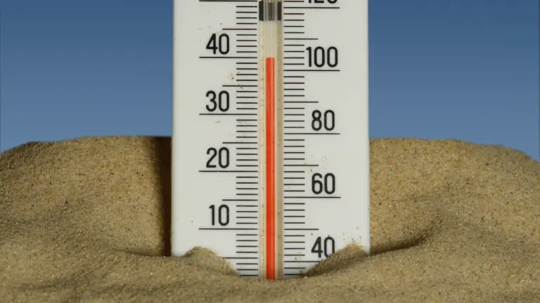 Ein Thermometer im Sand unter blauem Himmel zeigt hohe Temperaturen an.