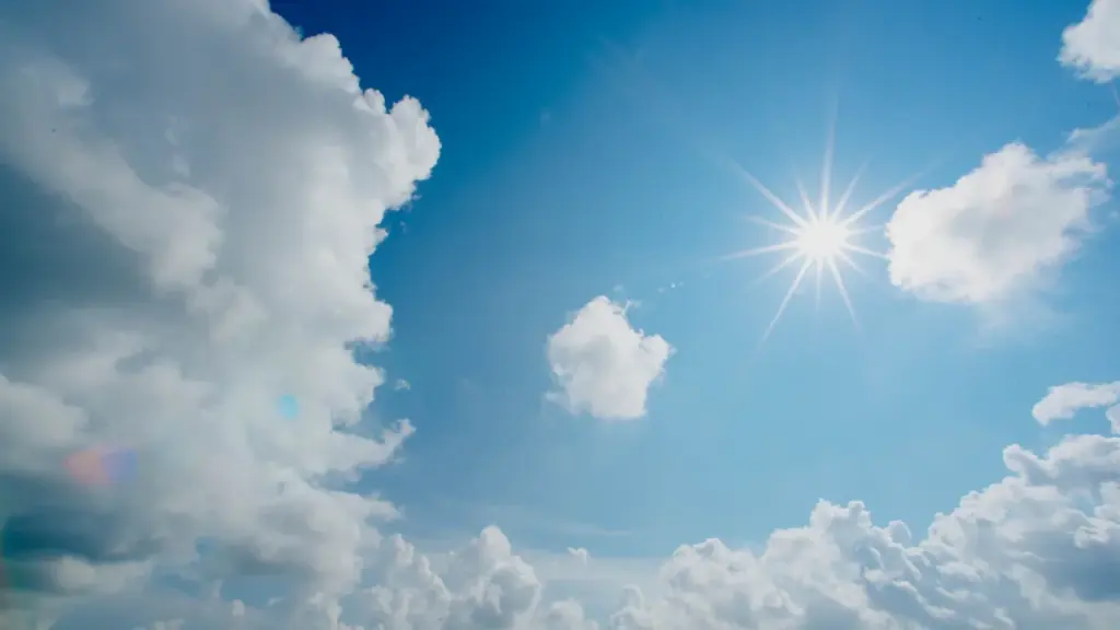 Heller blauer Himmel mit strahlender Sonne und vereinzelten weißen Wolken im Sommer.