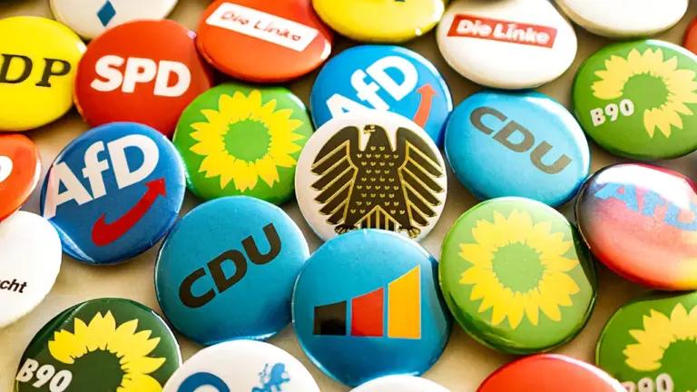 Verschiedene Anstecknadeln deutscher politischer Parteien liegen auf einem Tisch verteilt.