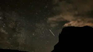 Eine Sternschnuppe leuchtet am nächtlichen Sternenhimmel über der Silhouette eines dunklen Berges.