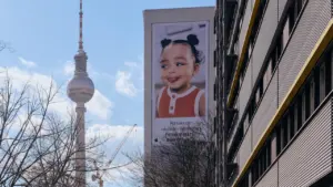 Der Berliner Fernsehturm überragt ein Gebäude mit einer Plakatwand eines fröhlichen Kindes.