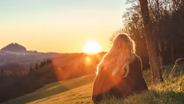 Eine Frau sitzt entspannt auf einer grünen Wiese und betrachtet den warmen Sonnenuntergang.