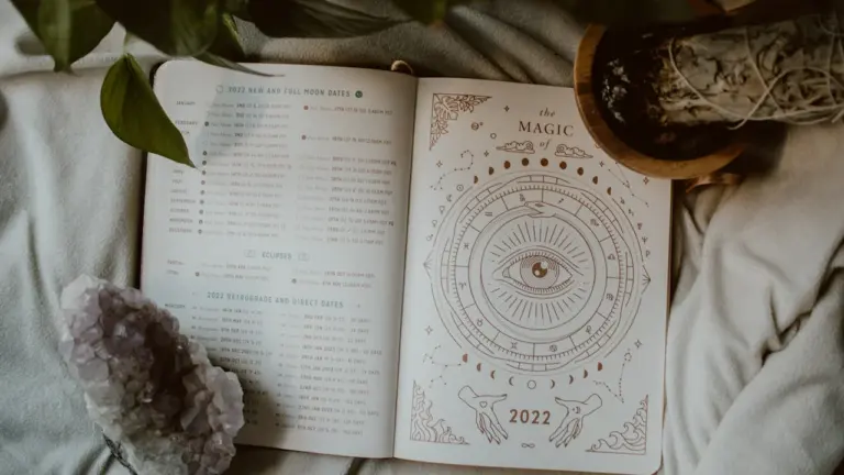 Ein offenes Buch mit astrologischen Symbolen und Kristallen auf einem bequemen Bett.