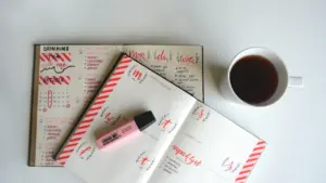 Offenes Notizbuch mit Kalenderwoche, Textmarkern und einer Tasse Kaffee auf dem Tisch.