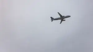 Ein graues Passagierflugzeug steigt in einen bewölkten, einfarbigen Himmel auf.