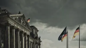 Blick auf das Berliner Reichstagsgebäude unter einem dramatisch bewölkten Himmel mit deutschen Flaggen.