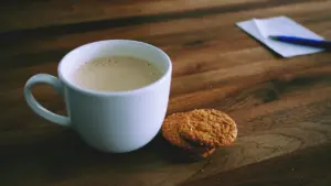 Eine weiße Kaffeetasse mit Keksen auf einem hölzernen Schreibtisch während einer Arbeitspause.