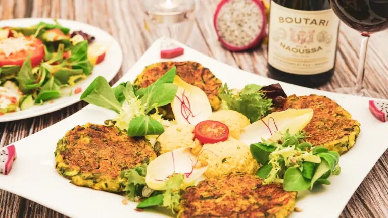 Knusprige Zucchinipuffer serviert mit frischem Salat und Dip auf einem weißen Teller.