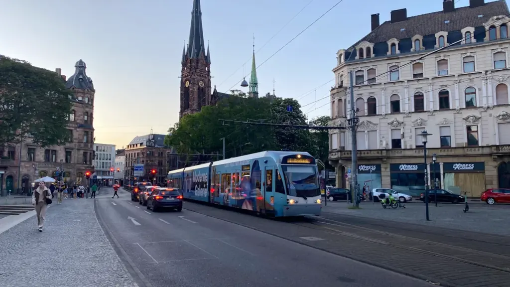 Eine Straßenbahn fährt durch die Stadt Saarbrücken an einer historischen Kirche vorbei.
