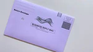 Ein hellvioletter Rückumschlag für US-Wahlen mit der Aufschrift Official Election Mail und Business Reply Mail.