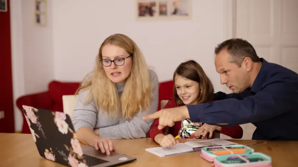 Eine Familie sitzt gemeinsam an einem Tisch und arbeitet konzentriert am Laptop zusammen.