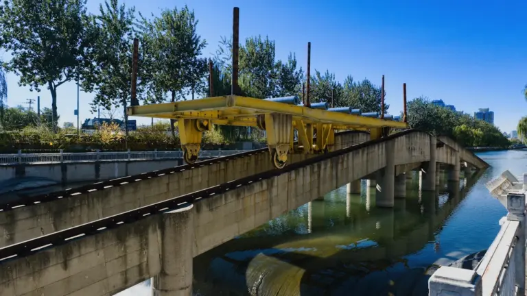 Gelbe Baumaschine auf einer Brücke über einem Fluss bei hellem Tageslicht.