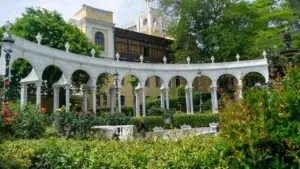 Weiße Arkaden und klassische Architektur in einem parkähnlichen Garten bei Tageslicht.