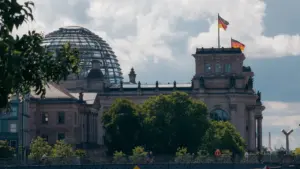 Das Reichstagsgebäude in Berlin mit wehenden deutschen Flaggen bei blauem Himmel.