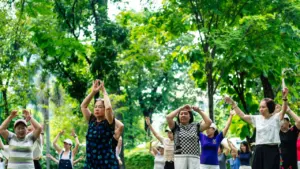 Eine Gruppe älterer Menschen führt gemeinsam gesundheitsfördernde Bewegungsübungen in einem grünen Park aus.
